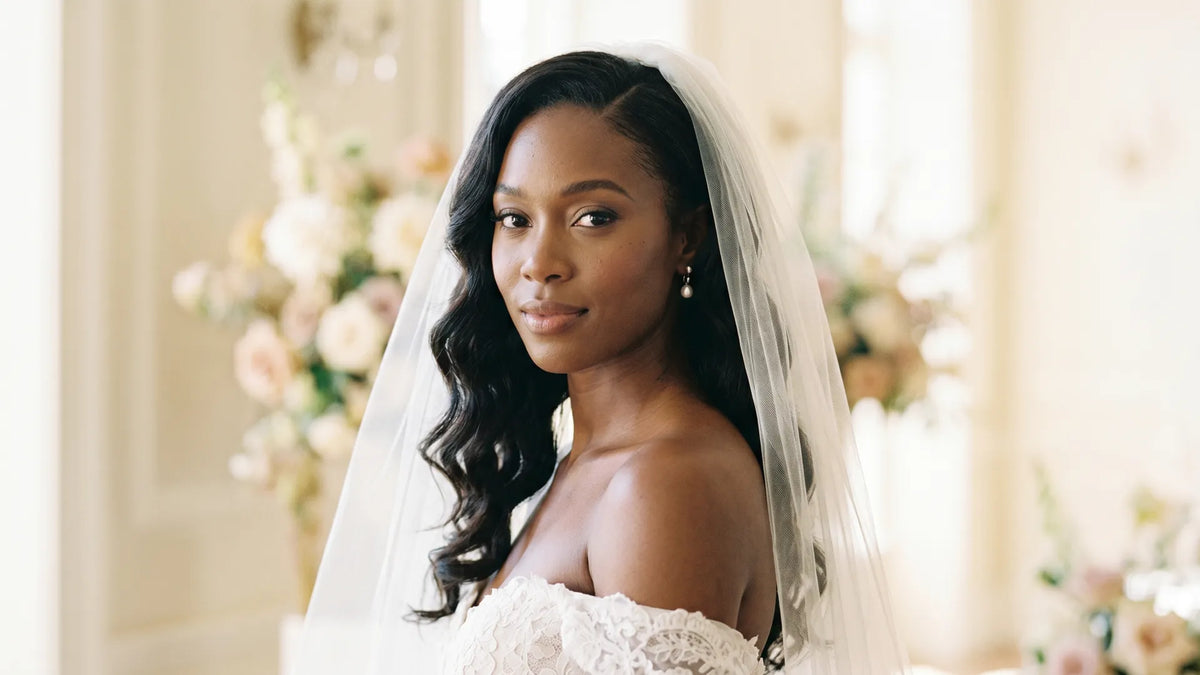 A beautiful bride in a white lace off-the-shoulder dress and veil, showcasing elegant long wavy hair styled with a Mimicing glueless wig.