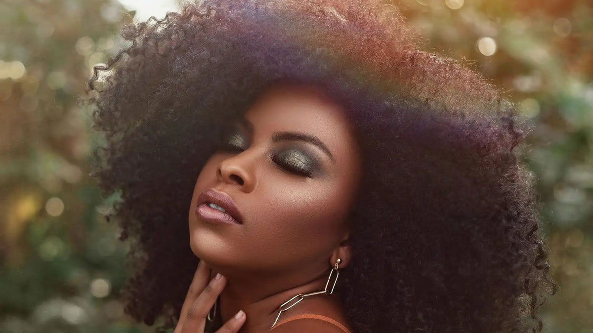 Elegant lifestyle portrait of a woman with voluminous natural kinky curly hair and glamorous makeup, showcasing a Mimicing glueless half wig in warm sunlight.